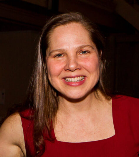 Portrait of Movement Research Executive Director, Barbara Bryan smiling. Her straight hair is down at shoulder level. She wears a sleeveless red dress. Photo by Alex Escalante.