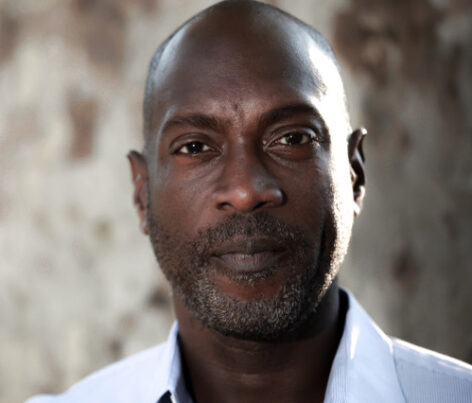 Portrait of Paul Hamilton from the shoulders up. he is a Jamaican born man with grey hairs in his mustache and chin. Photo by Daniel McKnight.