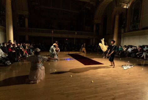 loveconductors performing at Movement Research at the Judson Church. Dancers are in motion executing different actions. One of them is squatting with arms to the side, another is in a gentle pelvic tilt body wrapped in fabric and fluorescent lights, at distance a dancer is walking with a big rope between the hands, another dancer swings a flowy fabric through the hair. Photo by Rachel Keane.