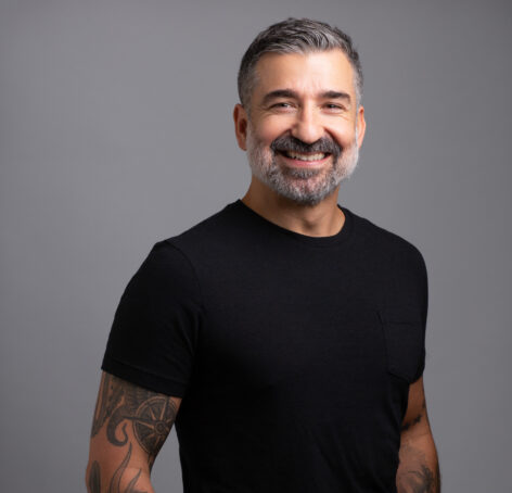 Photo of Fabio Tavares posing in a studio. He is wearing a black t-shirt and smiling into the camera. Photo courtesy of the artist.