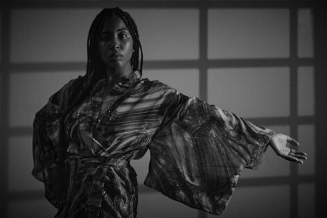 Black and white image of Megan Curet, arm extended to the left with right hand on hip. Photo courtesy of the artist.
