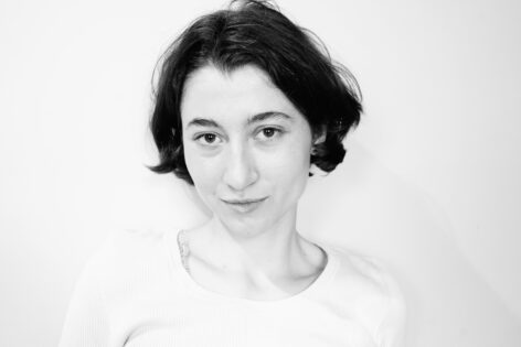 Portrait of Operations Intern Adèle Wester looking into the camera and smiling. The black and white photo captures her against a white background. She has her hair down and is wearing a white t-shirt. Photo courtesy of the artist.