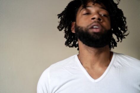 A caramel skinned black man is caught during a moment of movement and slightly out of focus. He is wearing a white v neck shirt and has textured hair. Photo by Amelia Golden