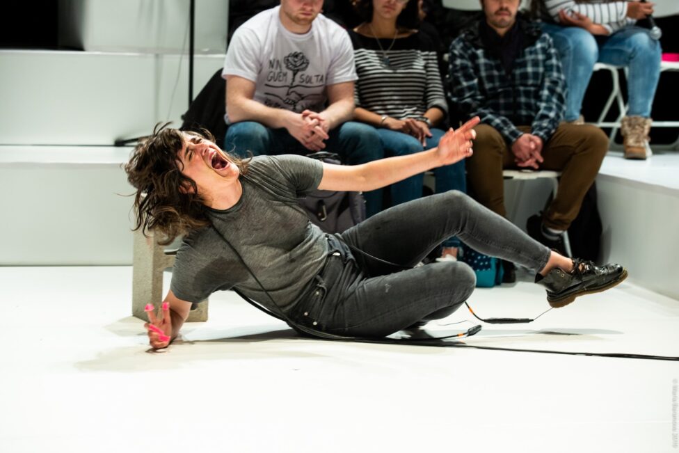 Faye Driscoll performing, wrapped in wires, with her mouth open wide.