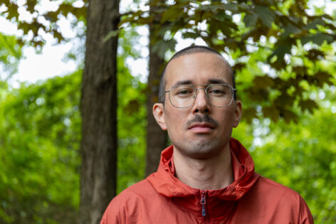 Glenn wearing a red jacket in the woods.Photo by evan ray suzuki.