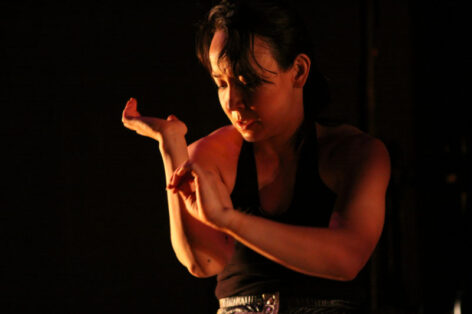 Maura in a orange light, she looks down at her wrist slightly bent. Photo by Steven Schreiber.
