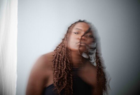 A blurred photo of a dark skinned Black femme with braids swinging her head. Photo by Thomas Dunn.