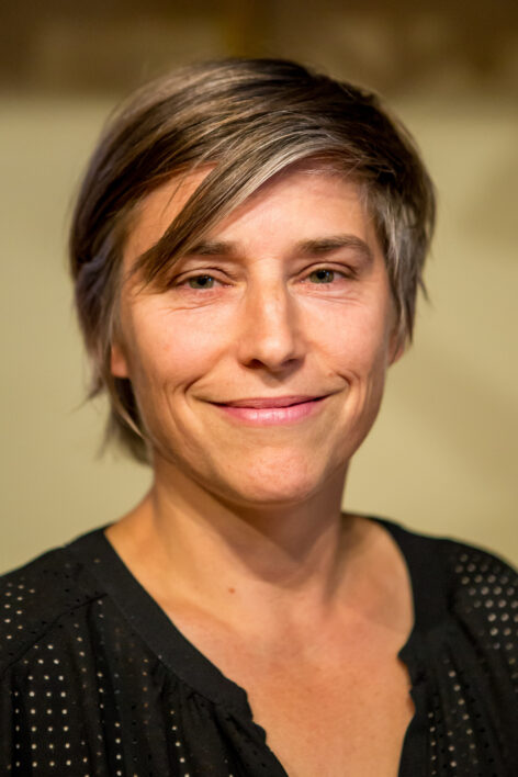 A portrait of a person smiling with short hair and black shirt. Photo by Peter Raper.