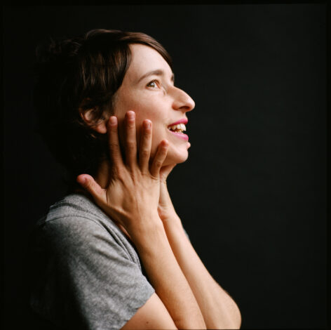 Performance photo of Tatyana Tenenbaum. She is dancing swaying her arms. She wears a blue and orange colorful top and has dark brown hair. Photo by Maria Baranova.