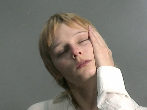 Sonya is in a white button down with their hand pressed against their face and their eyes closed. They have short blonde hair. Photo by Lavender Baths.