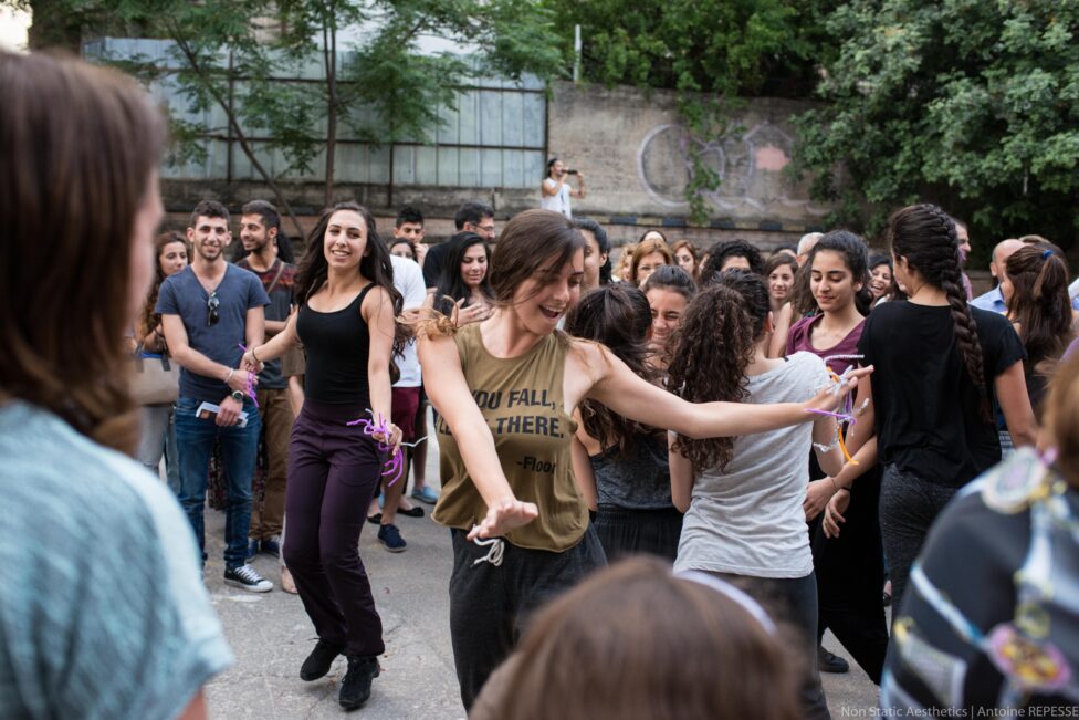 Joyful dancers emerge from the concrete, trees, and crowds, swinging their arms and smiling.