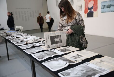 A table at MoMa with different issues of the Movement Research Performance Journal laid out. A person in a patterned sweater witha green coat draped over their arm looks through one. A table at MoMa with different issues of the Movement Research Performance Journal laid out. A person in a patterned sweater with a green coat draped over their arm looks through one. Photo by Paula Court.
