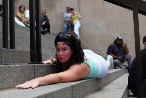 nibia lays on her stomach on a concrete stair underneath a handrail. Photo courtesy of the artist.