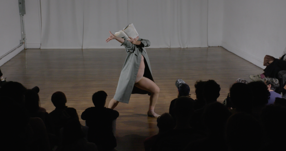 During a moment in Everything Must Go, Tess Dworman appears to be grasping for something from behind the front cover of a book which covers her face. Image by Kayhl Cooper.