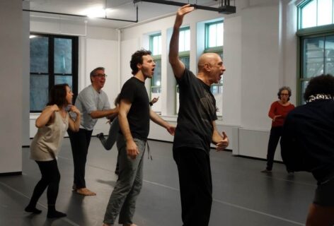 Several people stand around a circle inside of Movement Research's studio, gesturing in different ways and leaning forward with their tongues out. Photo by Harry Shunyao Zhang from the MR archives.