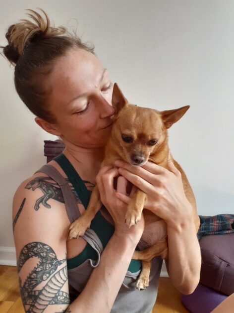 Catherine holding her dog Bambi up to her chest as she lowers her gaze in its direction 