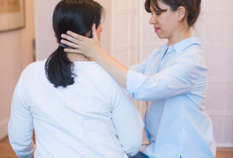 Anat is in session with a client. She sits next to the client and places her hands at either side of the clients lower jaw and neck. Photo by Elodie Saracco