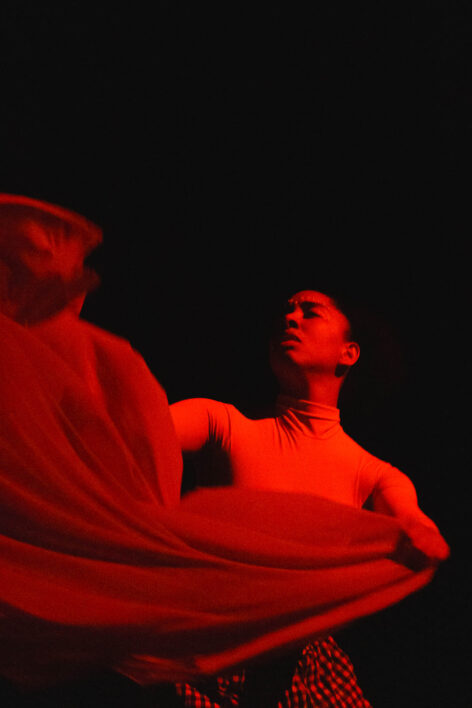 Dancer utilizing fabric through movement under red lit stage light. Photo by Jonathan Maier.