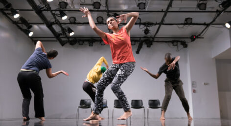 Photo of four dancers In
a black-box space.They are casually dressed. The performers are South Asian,Taiwanese, and Black. They dance in a circle, traveling backwards with arms spiraling. They move and swaying together. Photo by Asya Gorovitz.