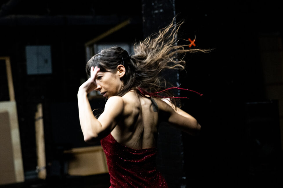 Wearing a deep red halter dress, Lisa Fagan performs in Deepe Darknesse, arms and hair thrown back. Photo credit to Maria Baranova.
