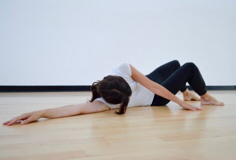 A bright studio. A dancer lays on the floor legs bent and arm reaching behind them. Photo by Rauschenberg Foundation