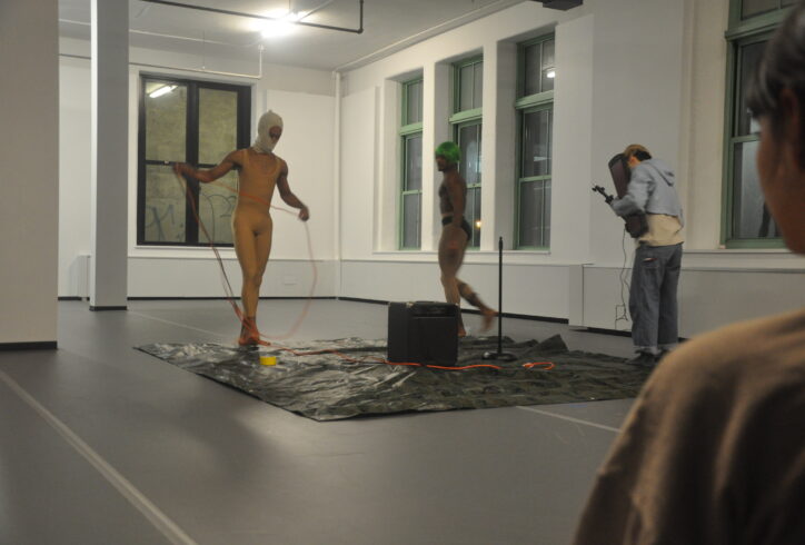 From the MR Archives: Open Performance. Three performers set up on a square tarp, they have cords and a large amp in the center of them. Artist Unknown. Photo by Mary Anne Bodnar.