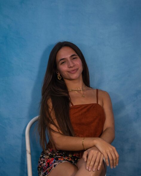 ID: Ana Teresa sitting down and smiling with hands crossed. Photo by @modelthe_