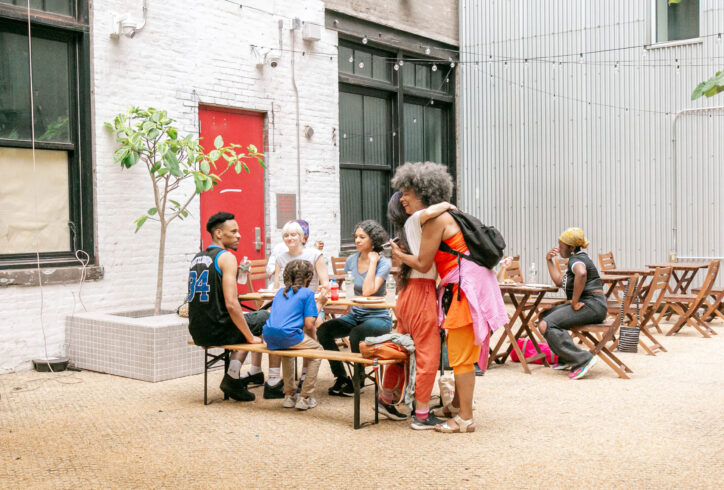 Photo by Aisha Williams. A photo of guests gathered at a table in the 122CC courtyard at the 2024 AoCC cookout.