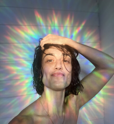 a person, devika, smiling in a selfie. there is a rainbow glow around them