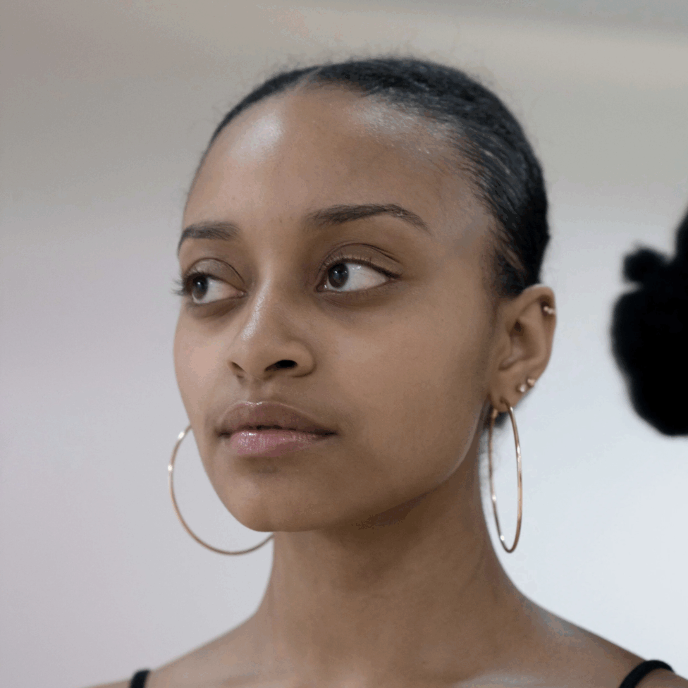Close-up portrait of Alysia with slicked-back hair and large hoop earrings, gazing left in soft studio light. Photo by Kevin Michael Briggs