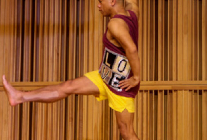 Gerald, a brown-skinned Filipino dancer, is wearing yellow shorts and a maroon tank top with the word LOVE emblazoned on it. He is kicking his right leg forward and stretching his right arm back. Photo by Julie Lemberger.