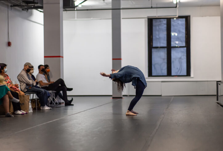 A photo of an Open Performance artist standing in a deep back bend reaching towards the onlooking audience. Photo by Rachel Keane