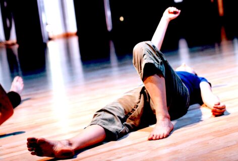 A person lays on the floor; one knee propped up and and one arm extended upward. Photo by Alex Gabrielli.