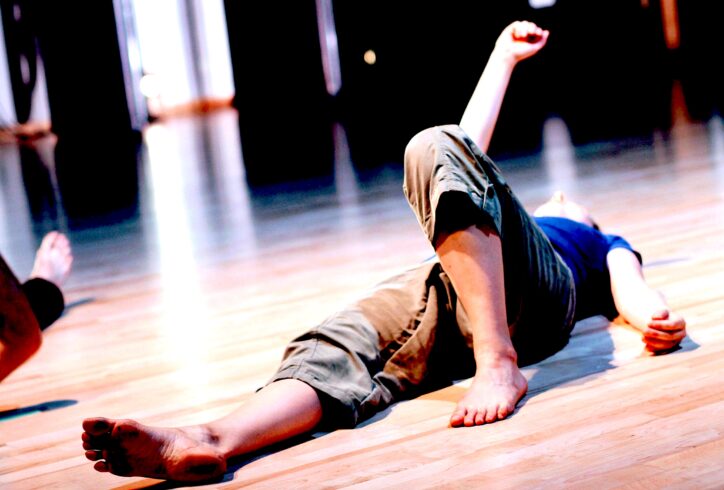A person lays on the floor; one knee propped up and and one arm extended upward. Photo by Alex Gabrielli.