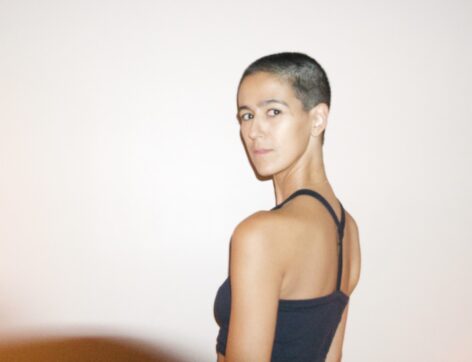 Roya, in a black tank top, looking over her shoulder at the camera. 