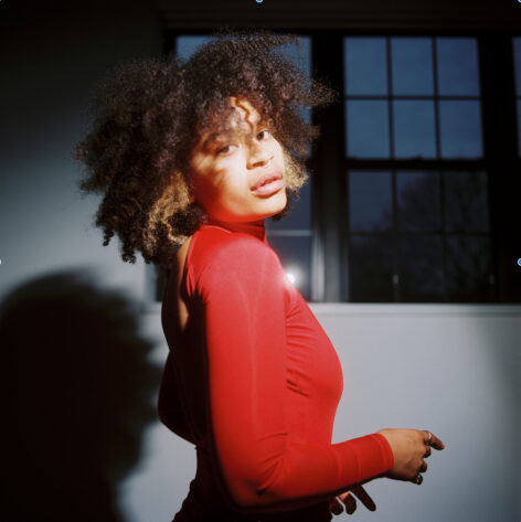 Portrait of dancer, Coco Villa, in a red leotard with large windows in the backdrop. Photo by Olu Okiemute.