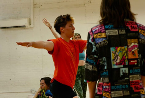 Juliana F May's class; a dancer with their arms out in T shape and one's back toward the lens, and another crouched behind. Photo by Amelia Golden