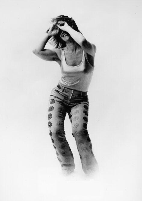 Iréne Hultman Monti standing with her arms covering her smiling face; she is wearing floral pants and a white tank top. Photo by Steve Ashmore.