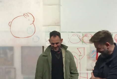 Jon Kinzel and Wally Cardona smiling and looking down as they stand in front of a wall covered with rabbit drawings. The wall is part of Jon Kinzel's project Atlantic Terminus at Invisible Dog in 2016.